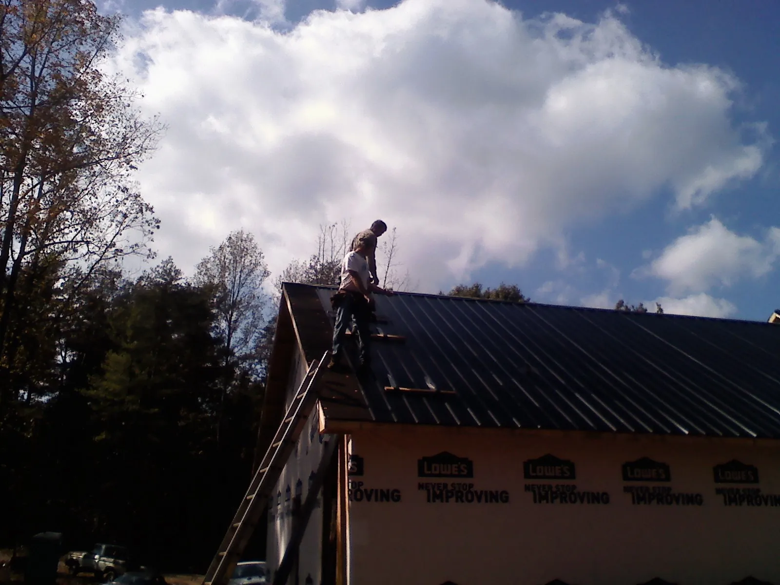 Roofer fastening dark metal panels high against a cloudy sky, from a Roof Inspection job in Enterprise